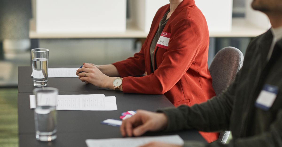 Election officials wearing name tags sitting at a table with documents and glasses of water indoors.